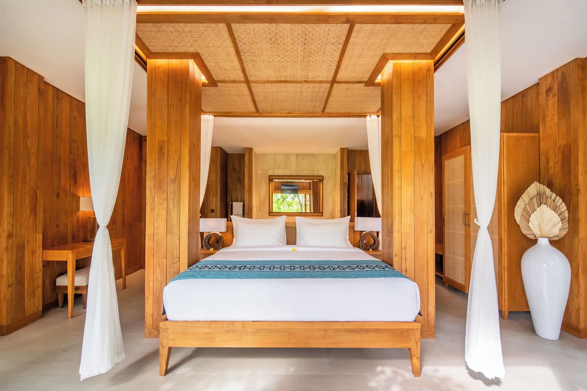 A wooden room with a bed, curtains, and a large vase.