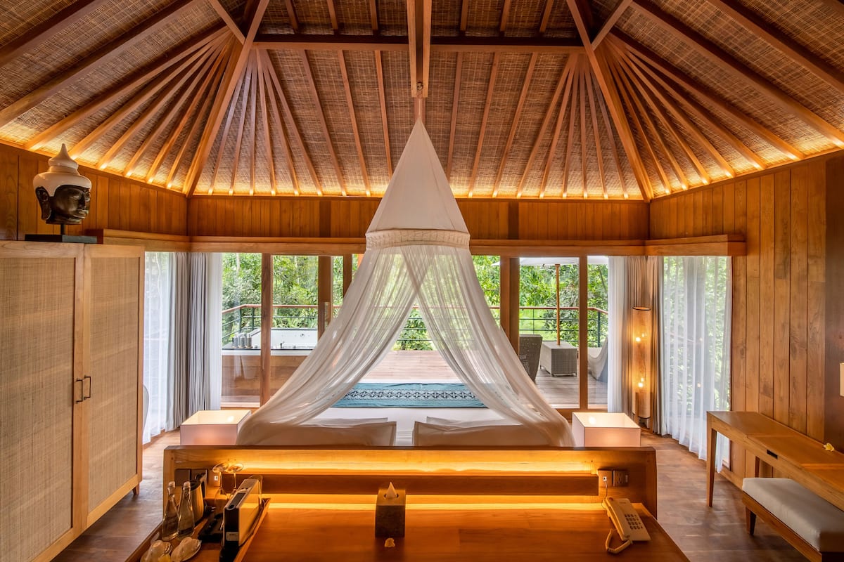A room with a canopy bed, wooden walls, and large windows.