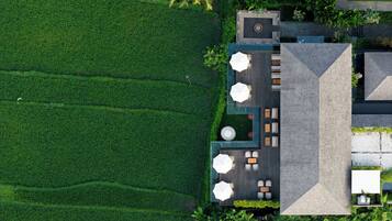 An aerial view of a resort with a rooftop terrace, lush green fields, and a modern building with outdoor seating.