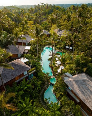 Un resort con varias edificaciones tipo bungalow, una piscina serpenteante y exuberante vegetación tropical.