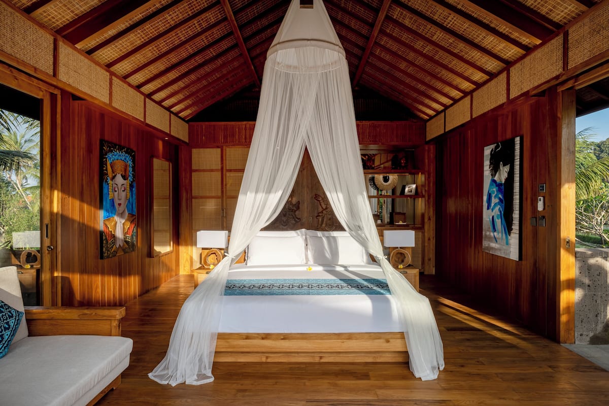 A room with a bed under a canopy, wooden walls, and a view of palm trees.