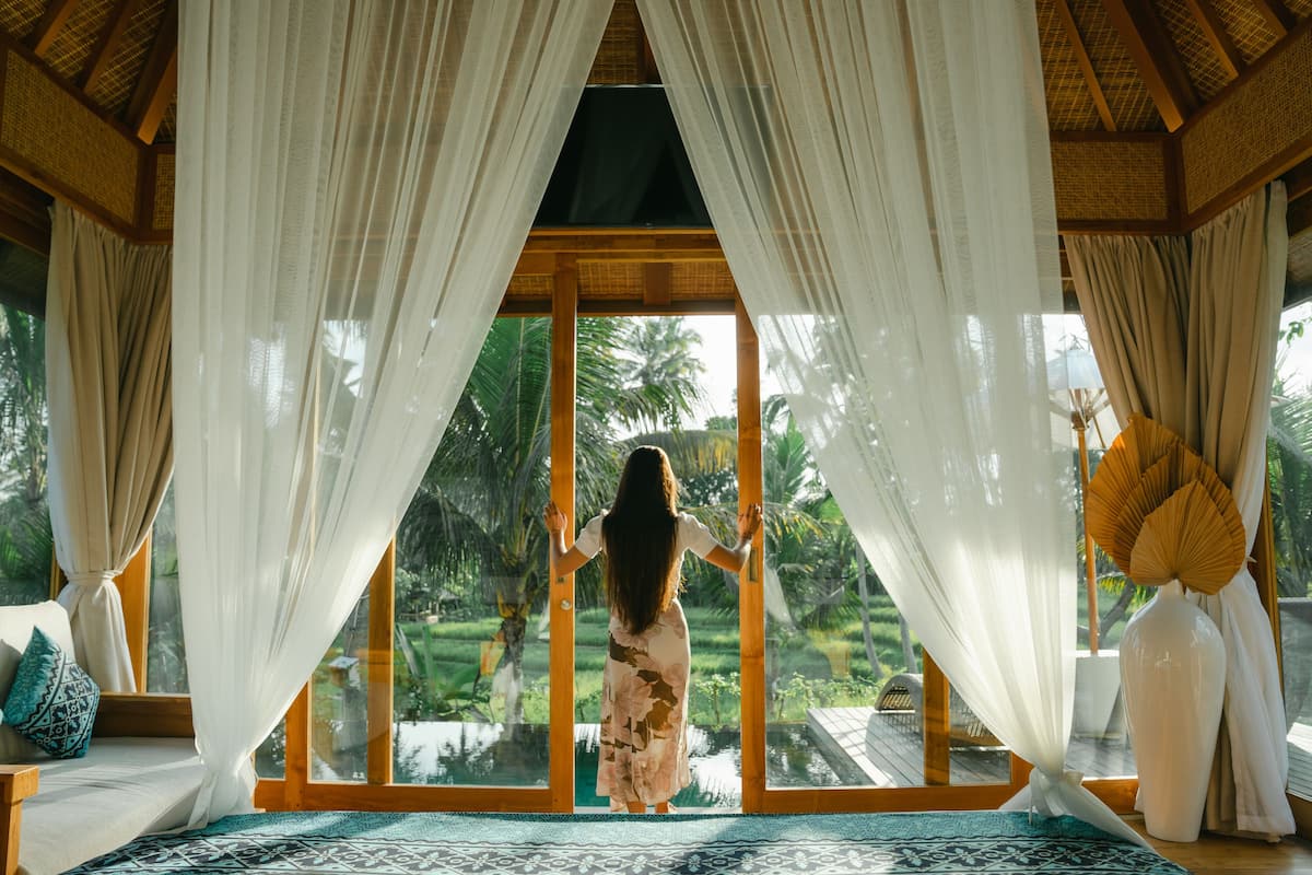 A room with a large window, a wooden ceiling, and a view of a tropical landscape.
