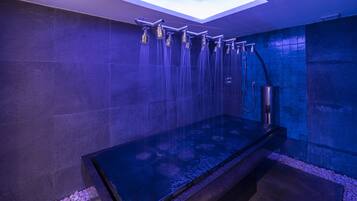 A modern bathroom with a glass-enclosed shower area, stone tiles, and a reflective floor.