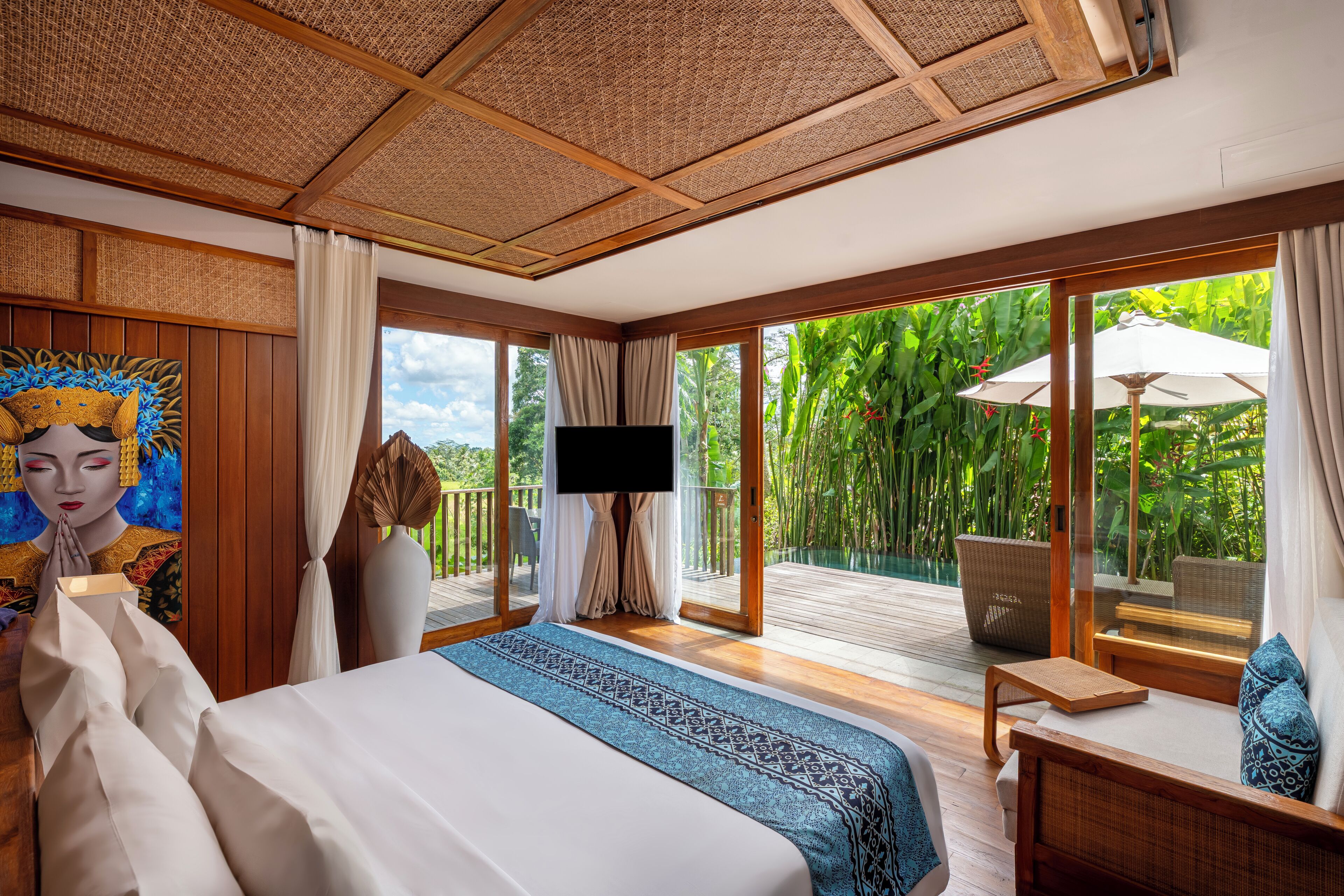 Een slaapkamer met een groot bed, een televisie, een balkon met uitzicht op groen en een eethoek met een tafel en stoelen.
