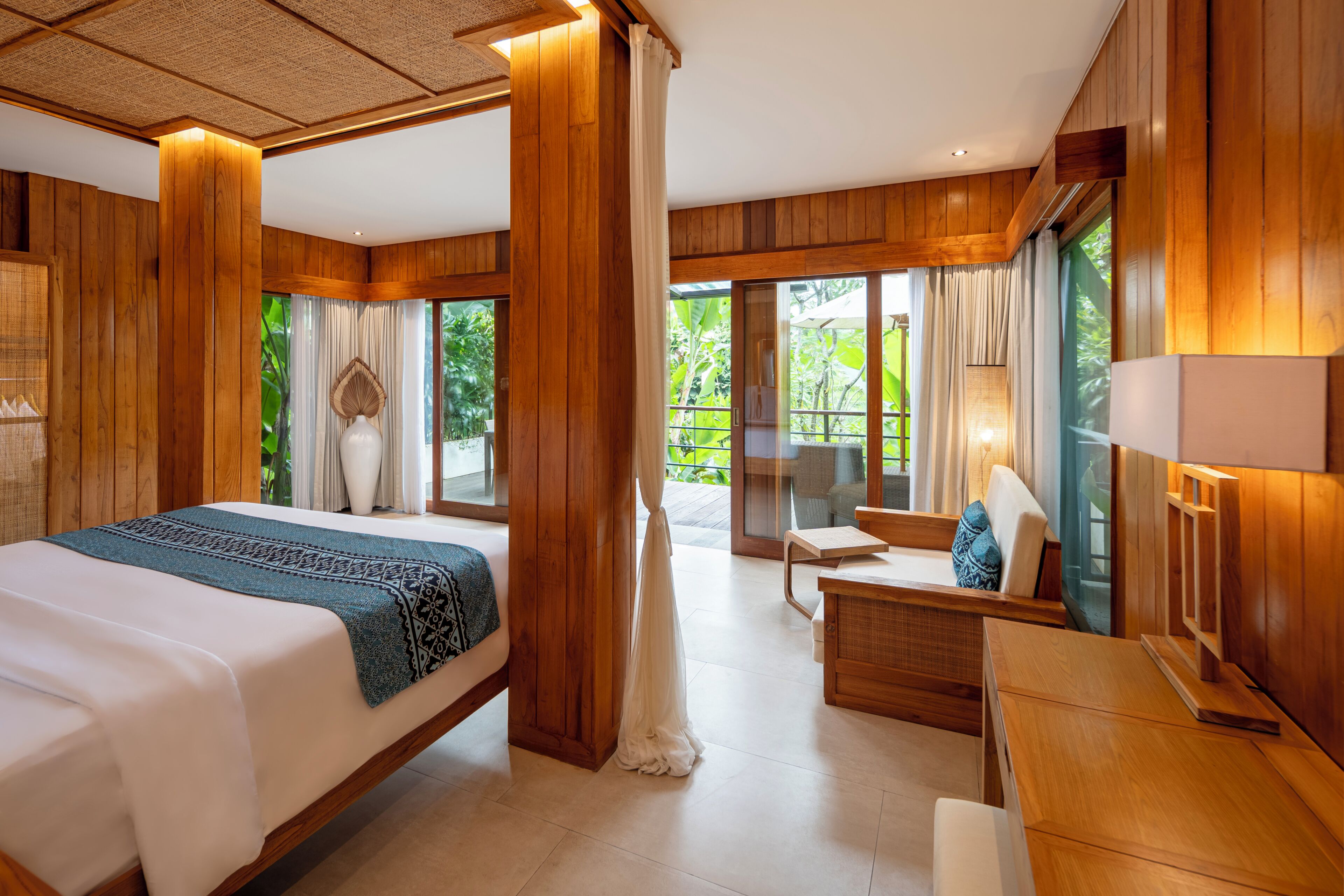 A hotel room with a bed, a desk, and a view of greenery outside.