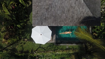 An aerial view of a house with a swimming pool, surrounded by lush greenery.