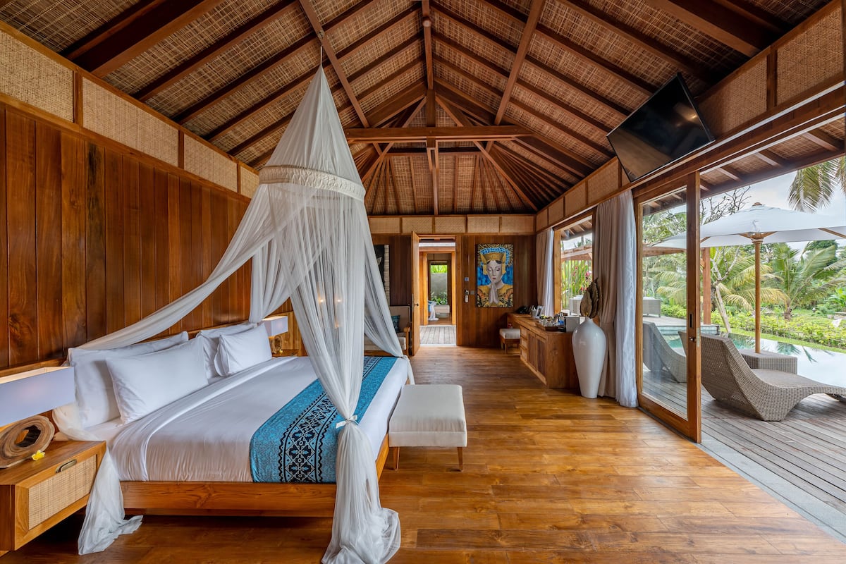 A spacious bedroom with a large bed, wooden walls, and a view of a pool.