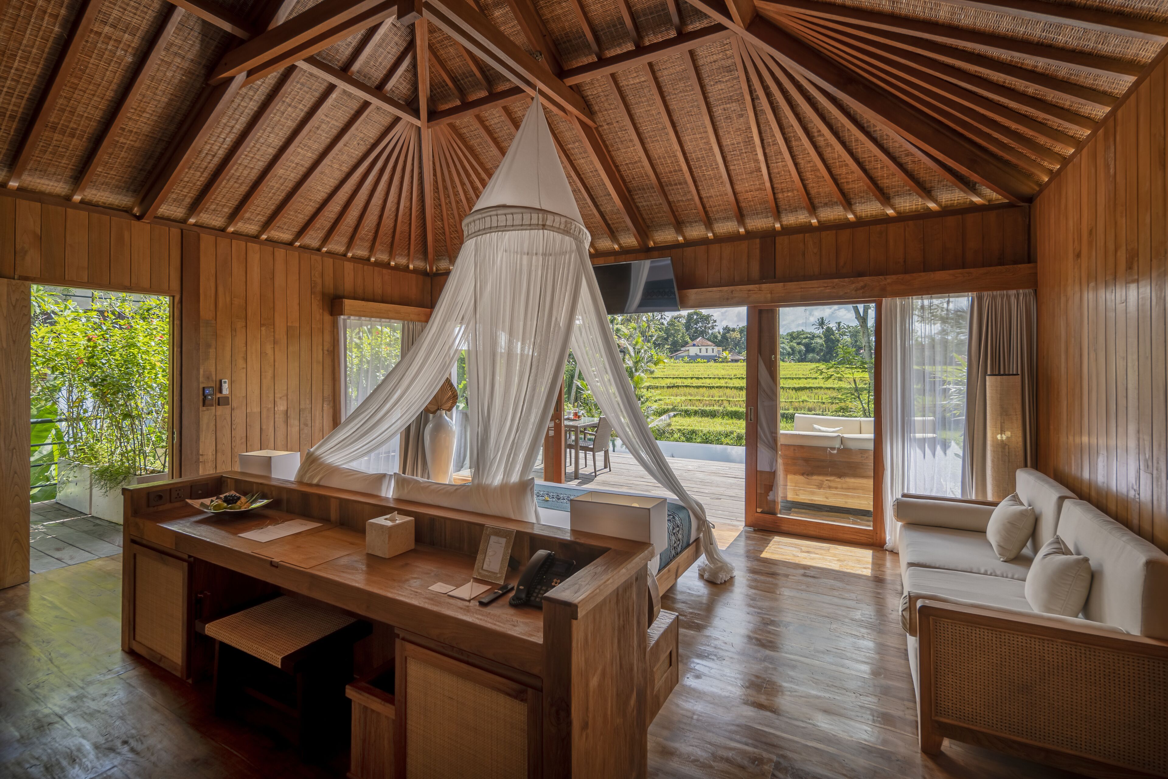 A wooden interior with a large desk, a sofa, and a canopy bed.