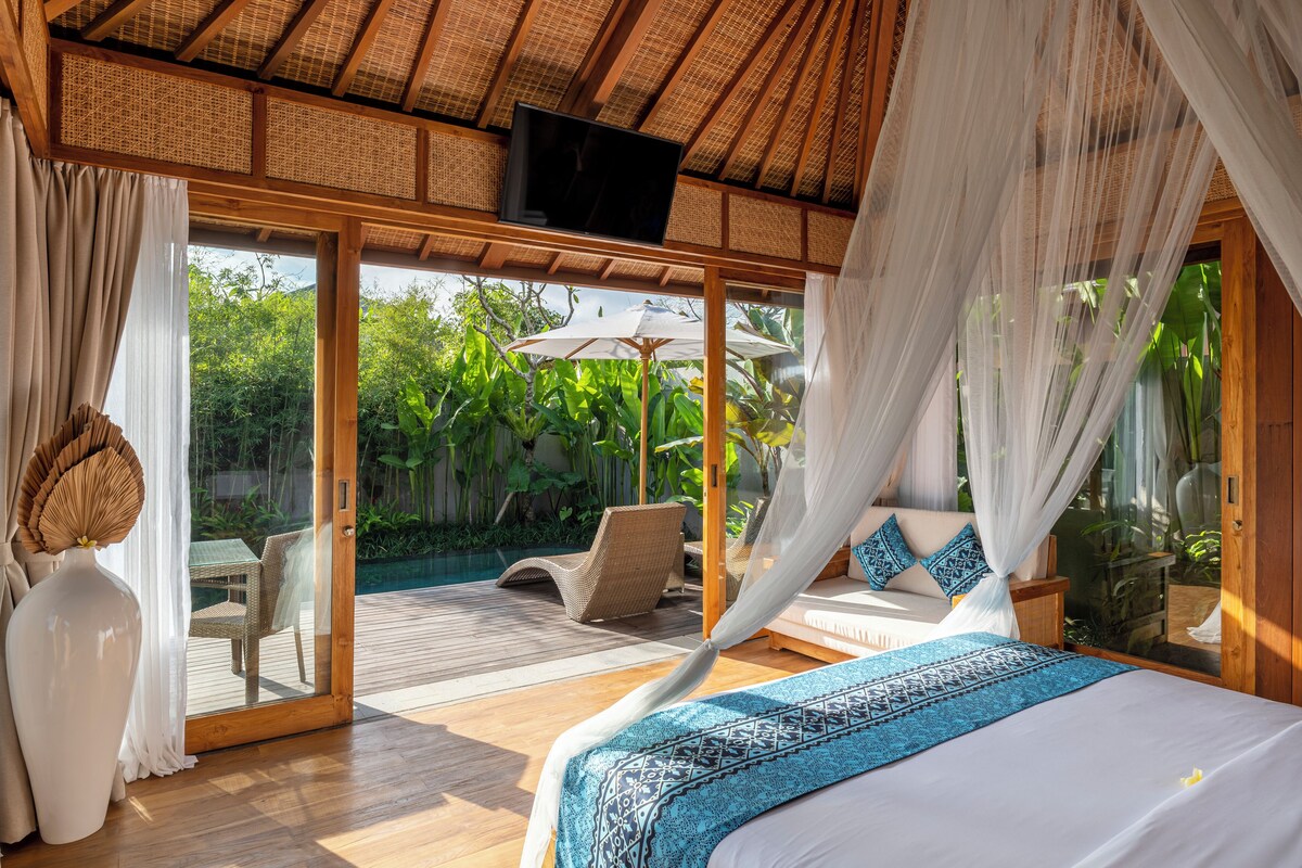 Un dormitorio con cama, cortinas, televisor y vistas a una piscina y zonas verdes.