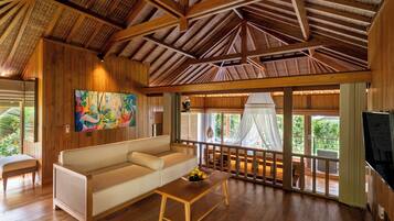 A wooden interior with a sofa, a coffee table with fruit, a painting, and a TV.