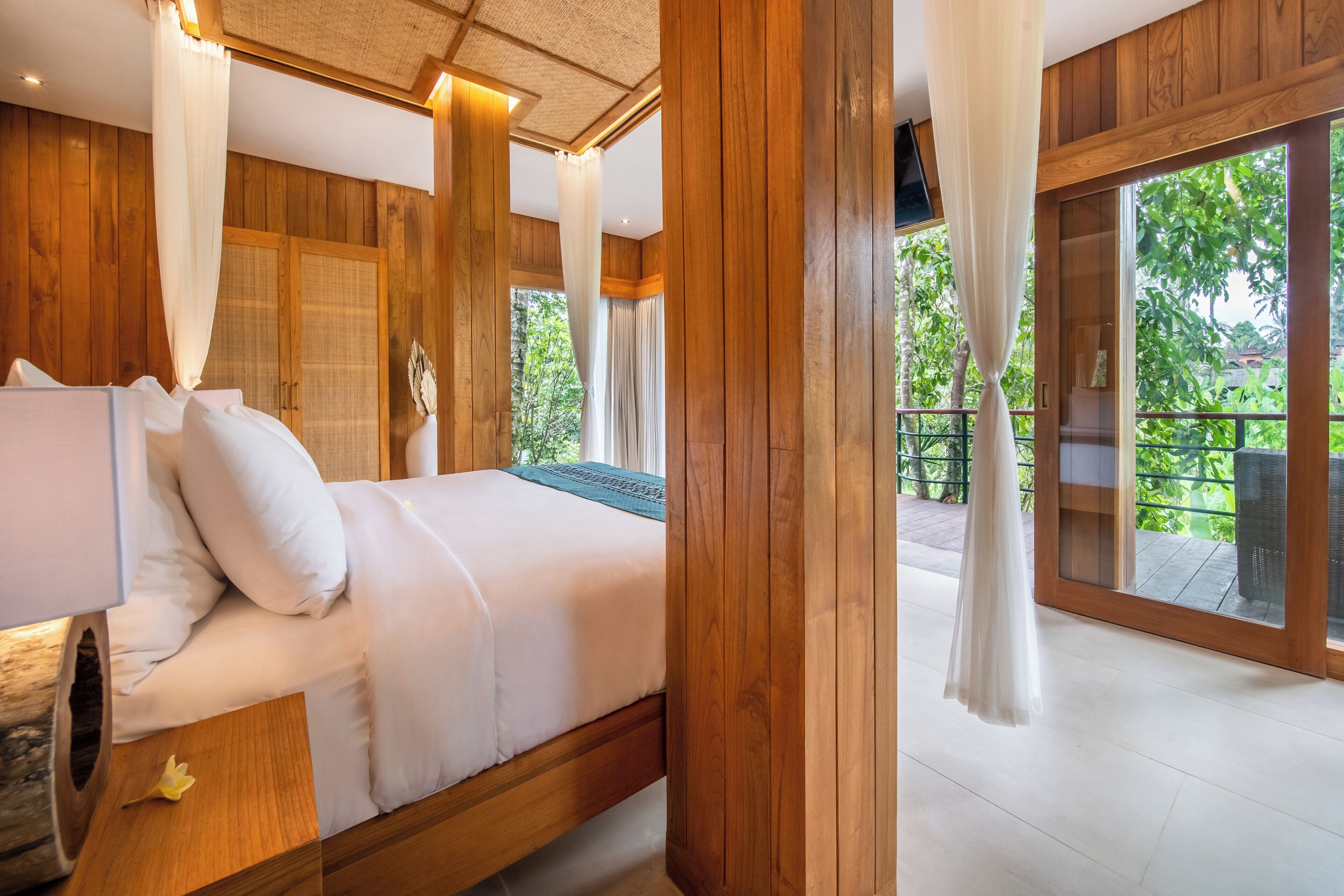 A bedroom with a wooden floor, a bed with white bedding, and a large window with curtains.