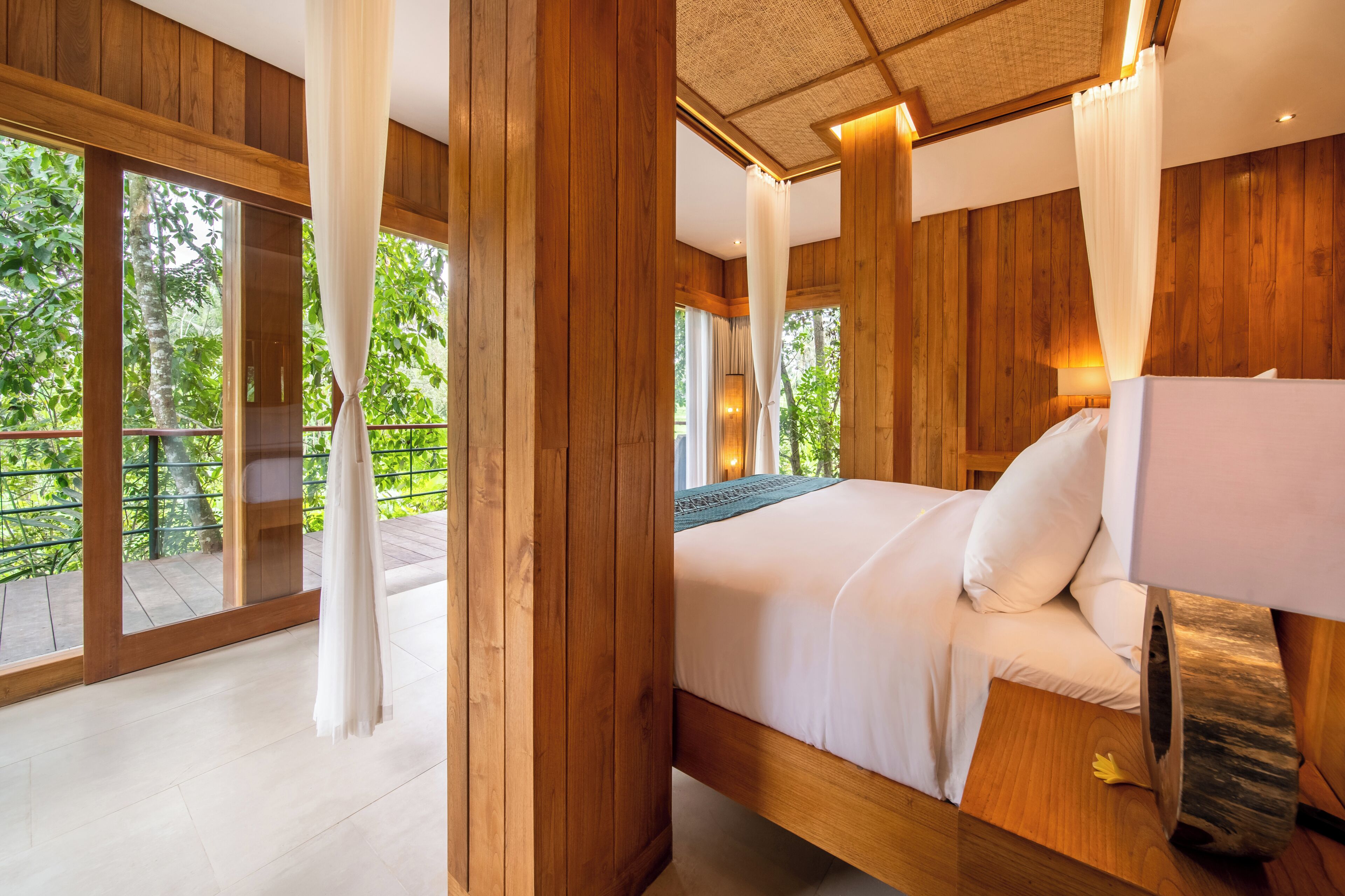 A wooden room with a bed, curtains, and a view of greenery.