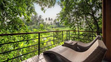 A wicker lounge chair on a wooden deck with a view of lush greenery and a distant landscape.