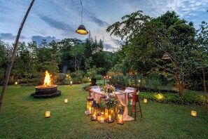 Un espacio al aire libre para comer con una chimenea, faroles y una mesa preparada para recibir a los invitados.