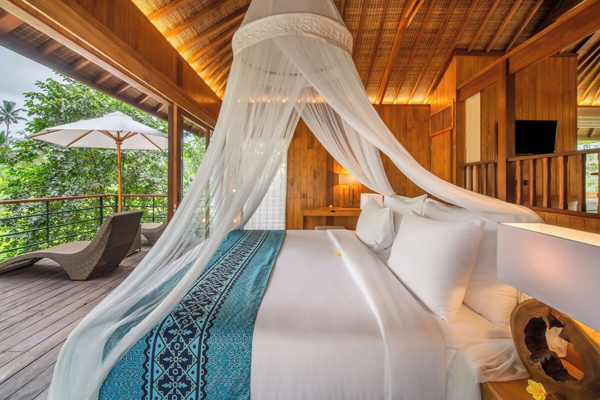Un dormitorio con cama con dosel, terraza de madera y vista a vegetación exuberante.
