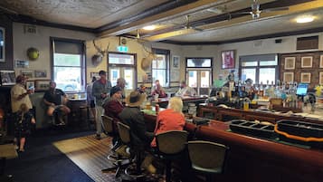 Un espace bar doté de nombreux tabourets et de tables, un comptoir avec une caisse enregistreuse, et un plafond orné de motifs décoratifs.