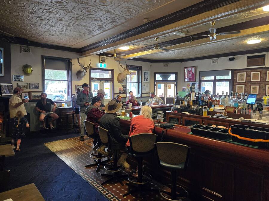 A bar area with multiple stools and tables, a counter with a cash register, and a ceiling with decorative patterns.