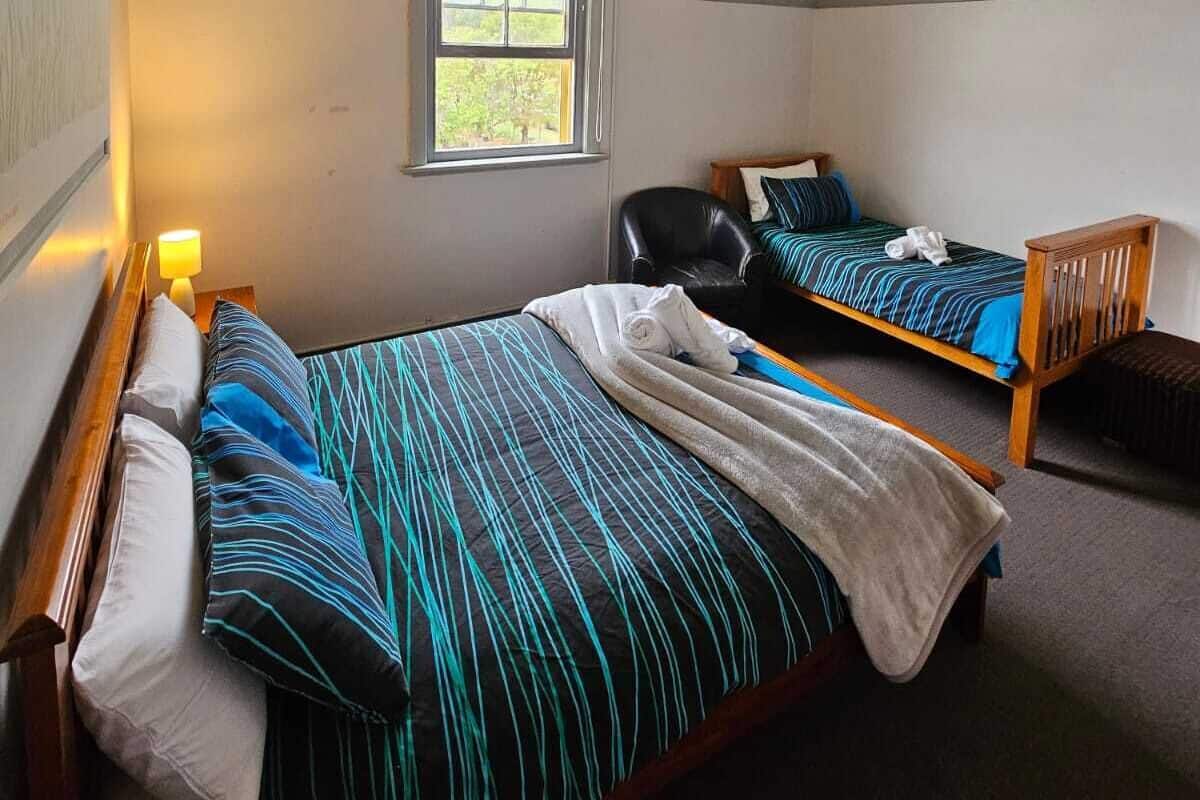 Una habitación con dos camas, una ventana, una silla y una lámpara.