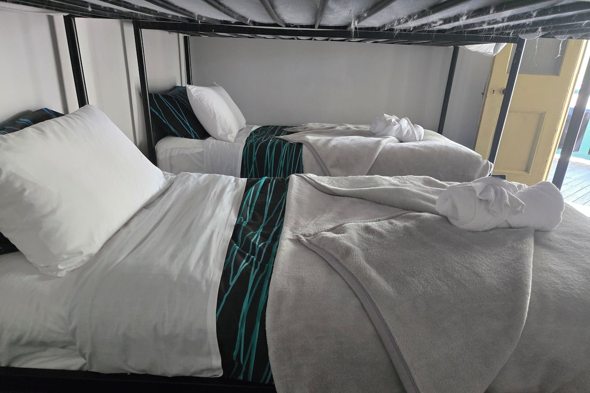 Una litera con ropa de cama a rayas blanca y aguamarina, una almohada blanca y una manta gris.
