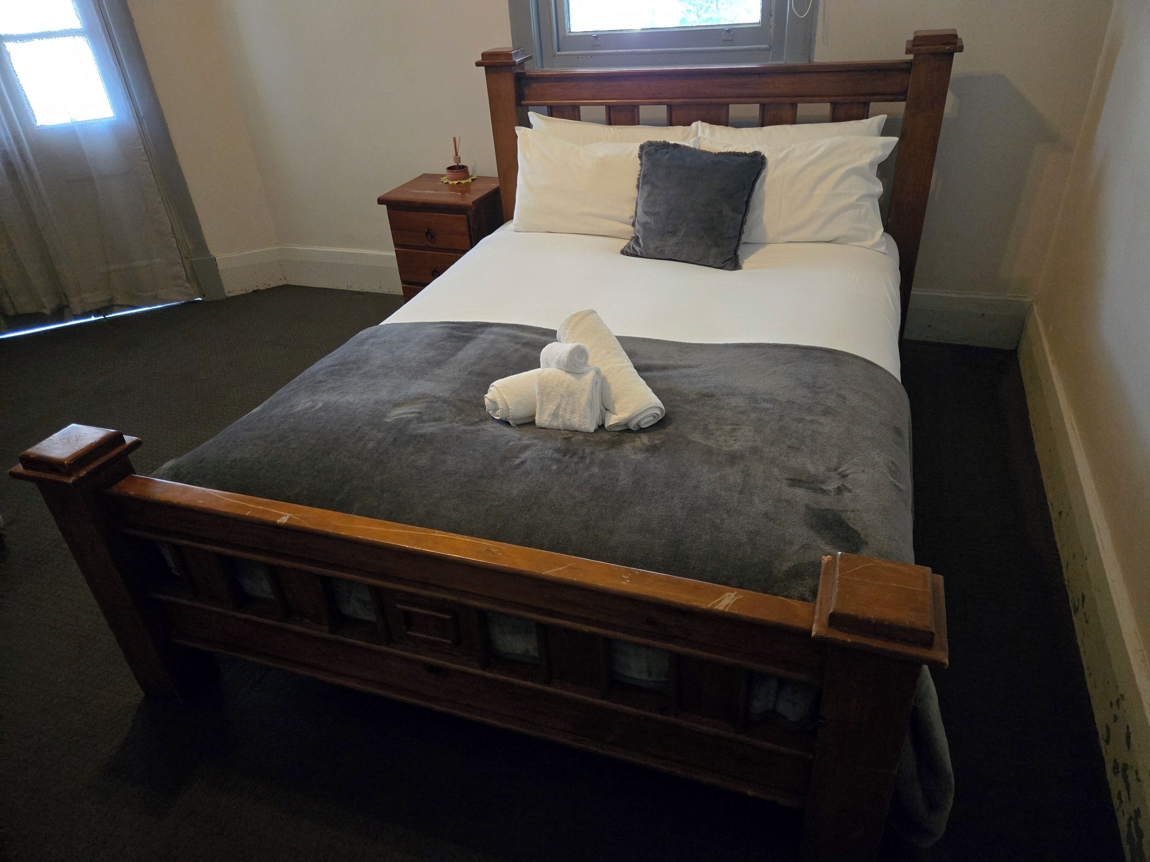 A neatly made bed with a grey blanket and two pillows, a wooden headboard, and a bedside table with a small decorative item.