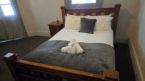 A neatly made bed with a grey blanket and two pillows, a wooden headboard, and a bedside table with a small decorative item. - Paxton Hotel (Paxton)