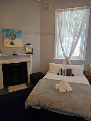 A hotel room with a bed, a fireplace, a window with sheer curtains, and a painting on the wall. - Paxton Hotel (Paxton)