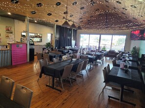 A restaurant with multiple tables and chairs, string lights, and a kitchen area visible in the background. - Paxton Hotel (Paxton)