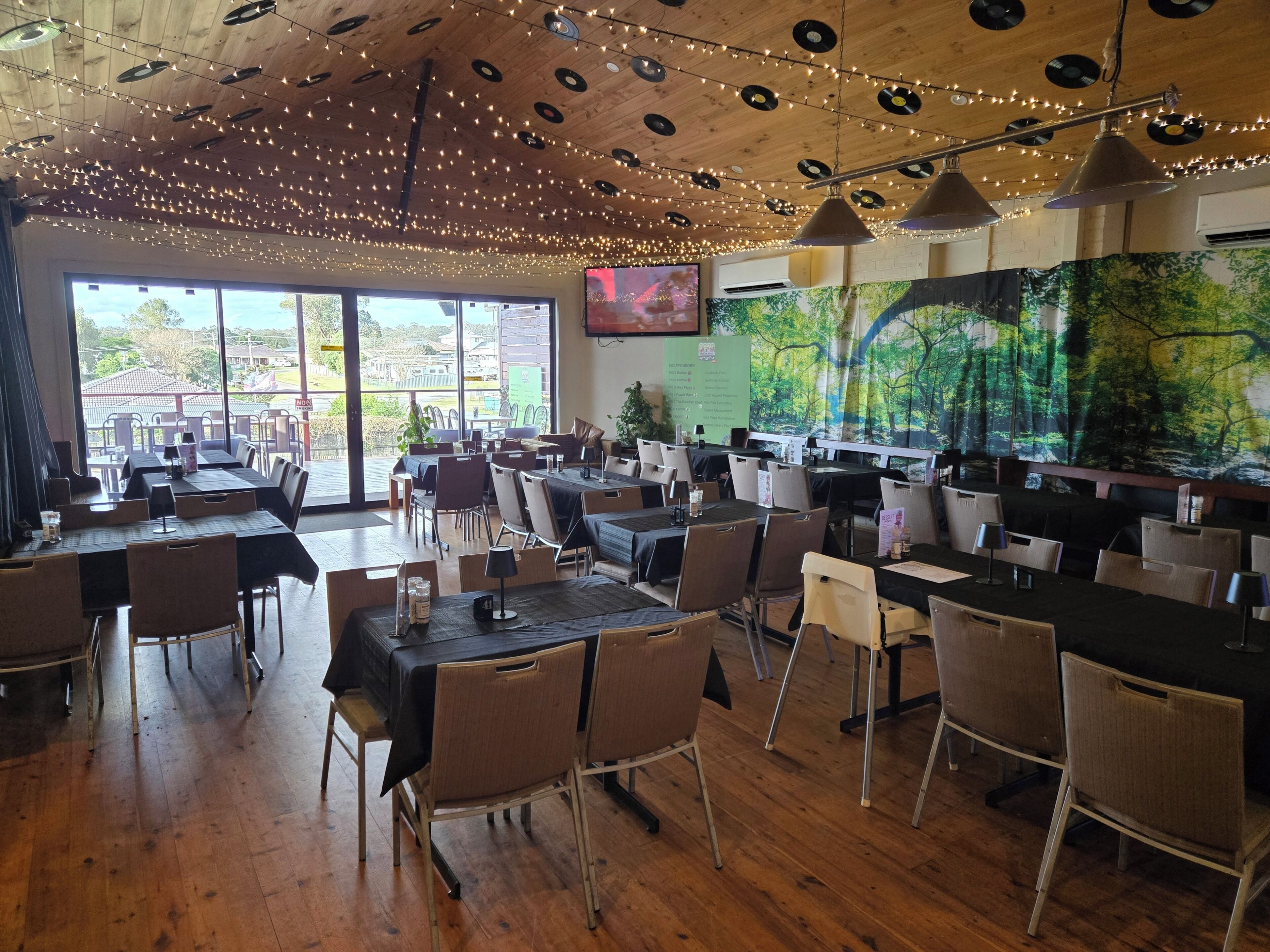 An indoor dining area with tables and chairs, wooden flooring, and string lights on the ceiling.