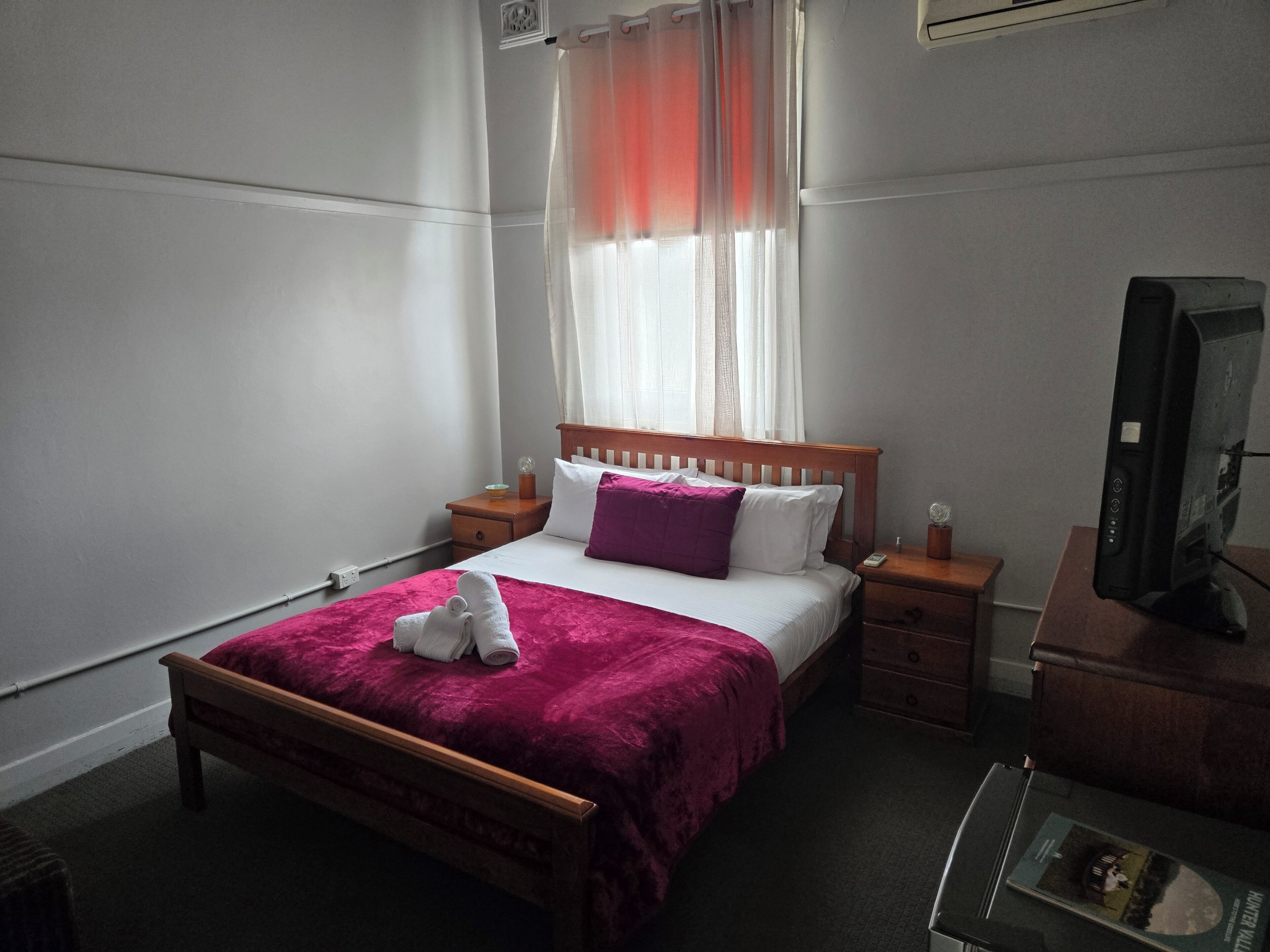 A hotel room with a bed, a nightstand, a television, and a window with curtains.