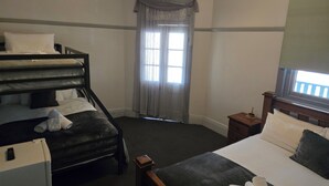 A room with bunk beds, a single bed, a window with curtains, a small table, and a television. - Paxton Hotel (Paxton)