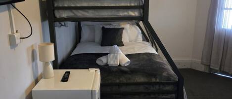 A bunk bed with a television mounted on the wall, a small refrigerator, and a bedside lamp.