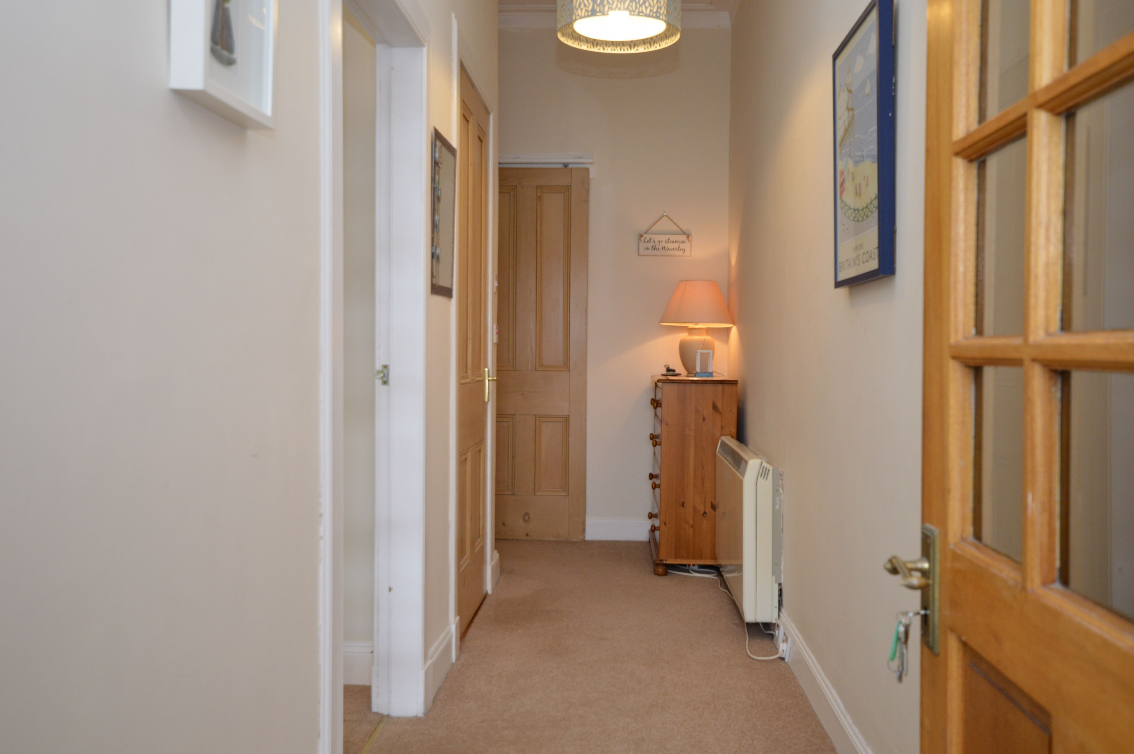 A hallway with a wooden door, a radiator, and a wall-mounted lamp.