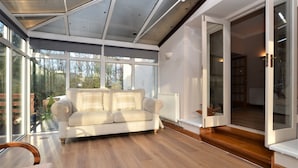 A modern living room with a sofa, wooden flooring, and large windows. - Kevington Cottage, charming one bedroom cottage, conservatory, decking area, (Dunoon)