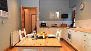 A kitchen with a wooden table set for dining, white cabinets, a microwave, a stove, and a clock on the wall. - Kevington Cottage, charming one bedroom cottage, conservatory, decking area, (Dunoon)