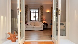 A room with a white sofa, a wooden floor, a window with curtains, and a lamp. - Kevington Cottage, charming one bedroom cottage, conservatory, decking area, (Dunoon)