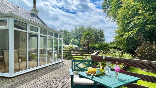 A conservatory with glass walls, a wooden deck, and a table with fruits and flowers. - Kevington Cottage, charming one bedroom cottage, conservatory, decking area, (Dunoon)