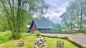 A rustic cabin with a sloped roof, surrounded by lush greenery and a wooden fence. - Iona Lodge, loch views, peaceful location, pet friendly (Taynuilt)