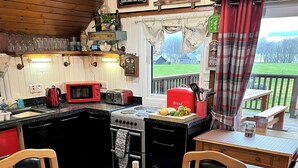 A cozy kitchen with a red microwave, a gas stove, and a sink. There are chairs and a table with a bottle of wine on it. - Iona Lodge, loch views, peaceful location, pet friendly (Taynuilt)