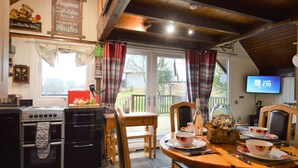A cozy kitchen with a wooden table set for dining, a television, and a sign about happiness being a kitchen full of smiles. - Iona Lodge, loch views, peaceful location, pet friendly (Taynuilt)
