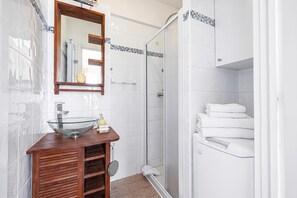 A bathroom with a glass bowl sink, wooden vanity, white tiles, a shower enclosure, and a mirror.