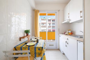 A small kitchen with a dining table, a potted plant, and a view of a building through a door.