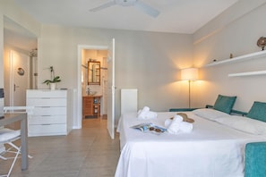 A hotel room with a bed, a desk, a chair, a dresser, a mirror, a lamp, and a ceiling fan.