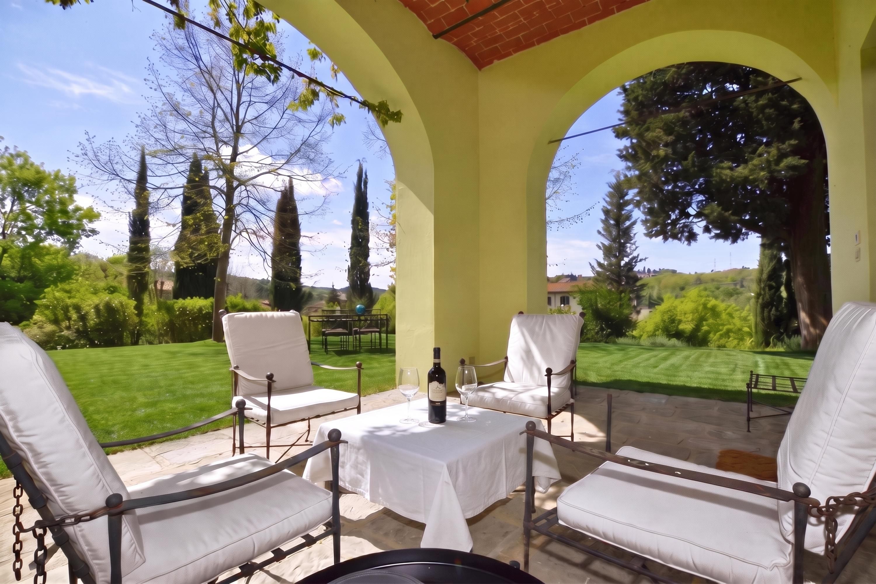 Une terrasse avec des chaises blanches dotées de coussins et une table, le tout agrémenté d’une pelouse bien entretenue et d’arbres en arrière-plan.
