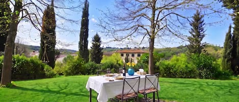 An outdoor dining area with a table set for two, surrounded by greenery and trees.