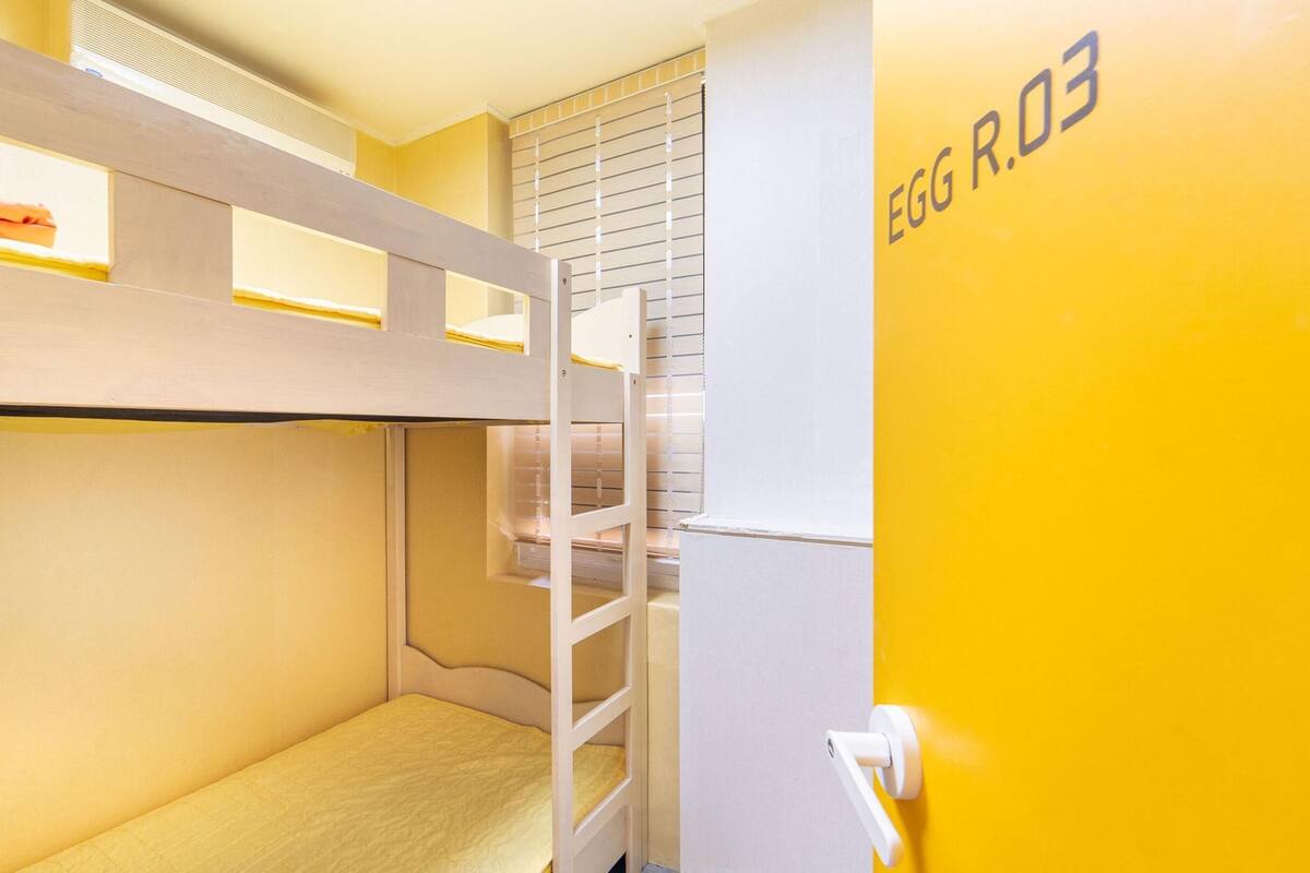 Une chambre avec des lits superposés, dont la porte blanche porte l’inscription « EGG R.03 ».