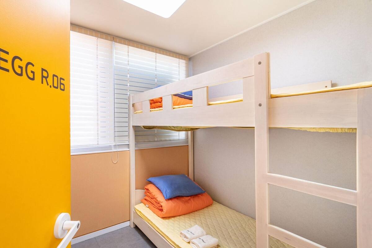 Une chambre avec un lit superposé, une fenêtre, une porte avec une poignée et un mur orné de texte.