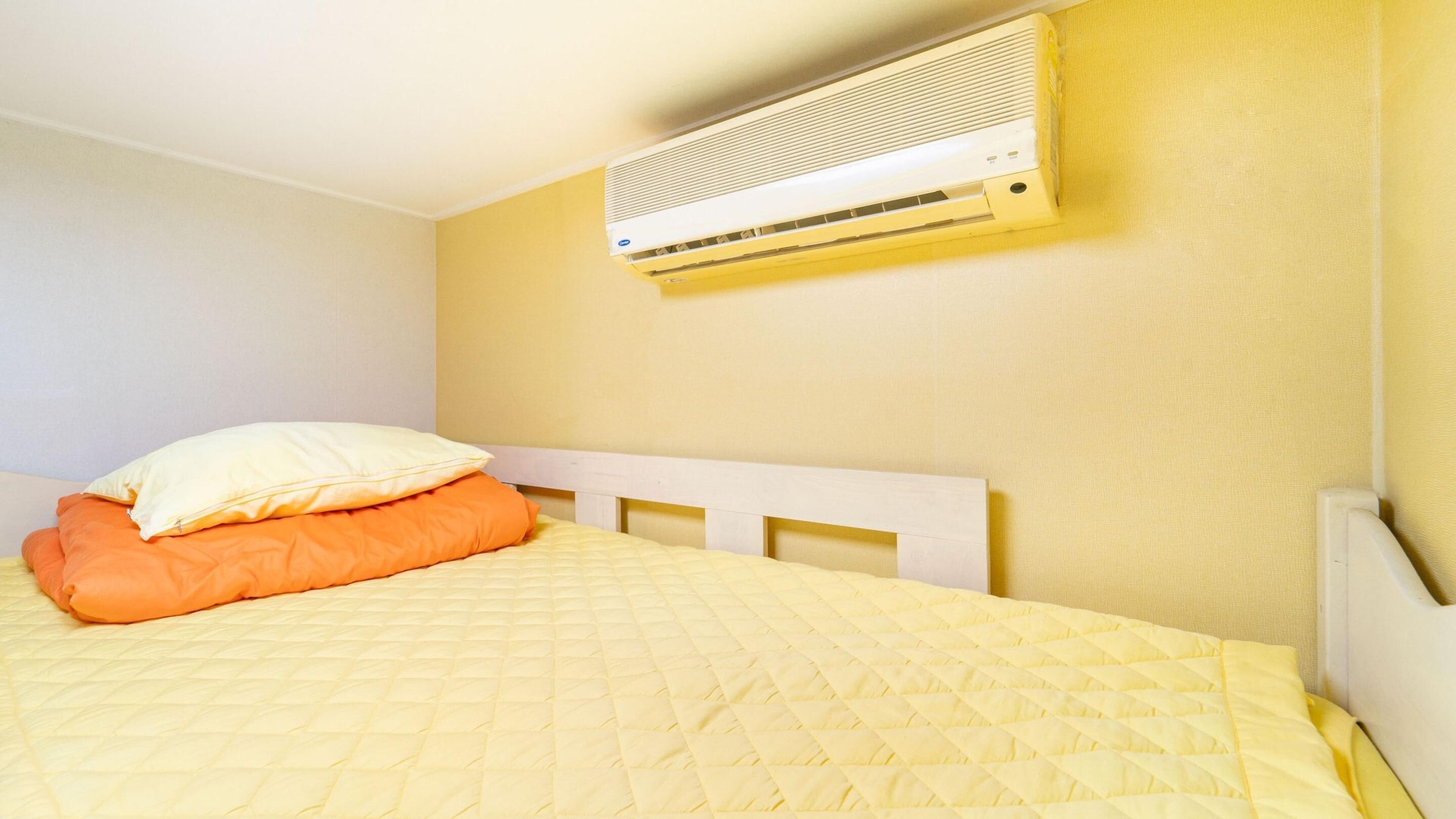 Uma cama com edredom acolchoado amarelo, um travesseiro laranja e um travesseiro branco.