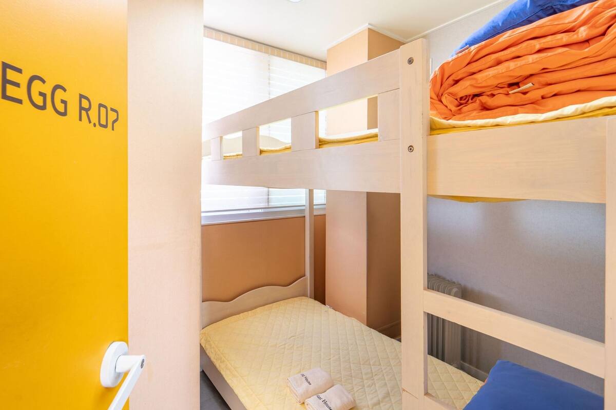 Une chambre avec un lit superposé, un mur jaune et un lit superposé avec une literie orange.