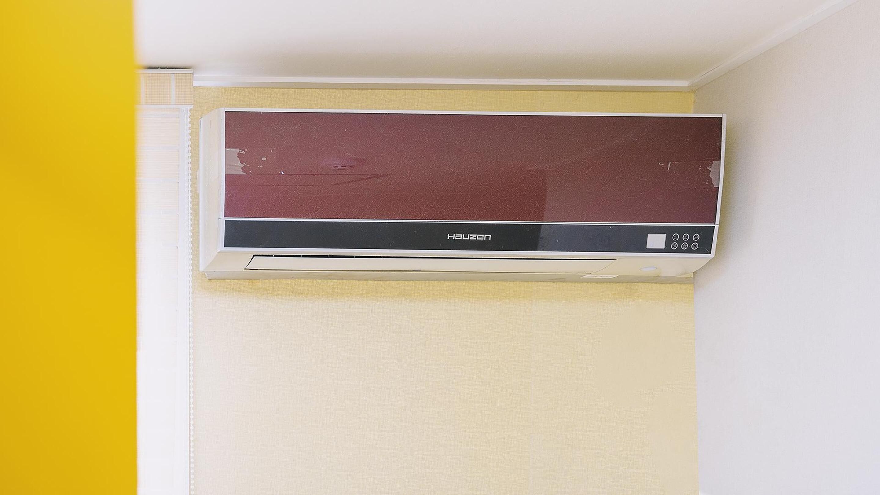 A wall-mounted air conditioner with a control panel, mounted on a wall with a yellow and white color scheme.