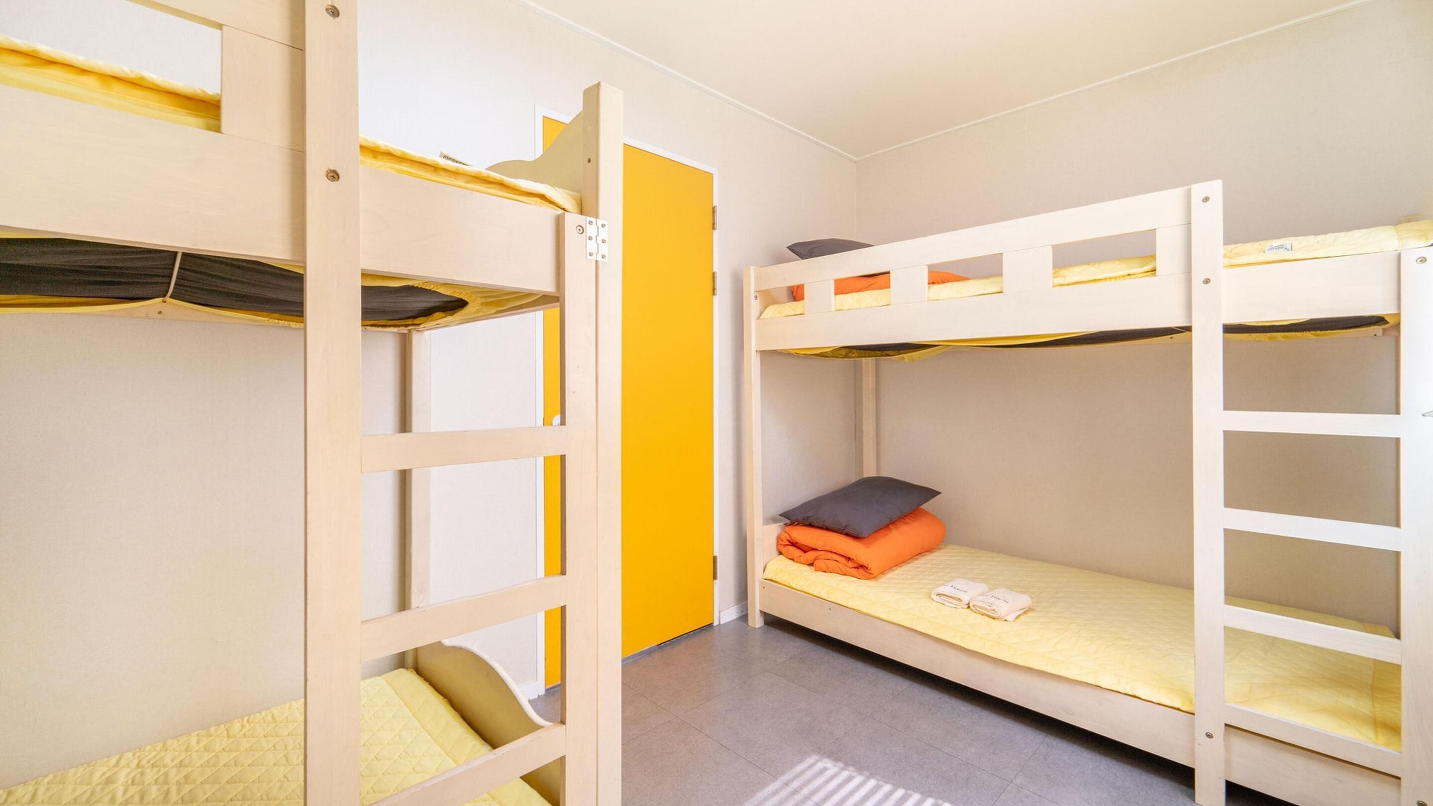 A dormitory room with bunk beds, a yellow door, and a tiled floor.